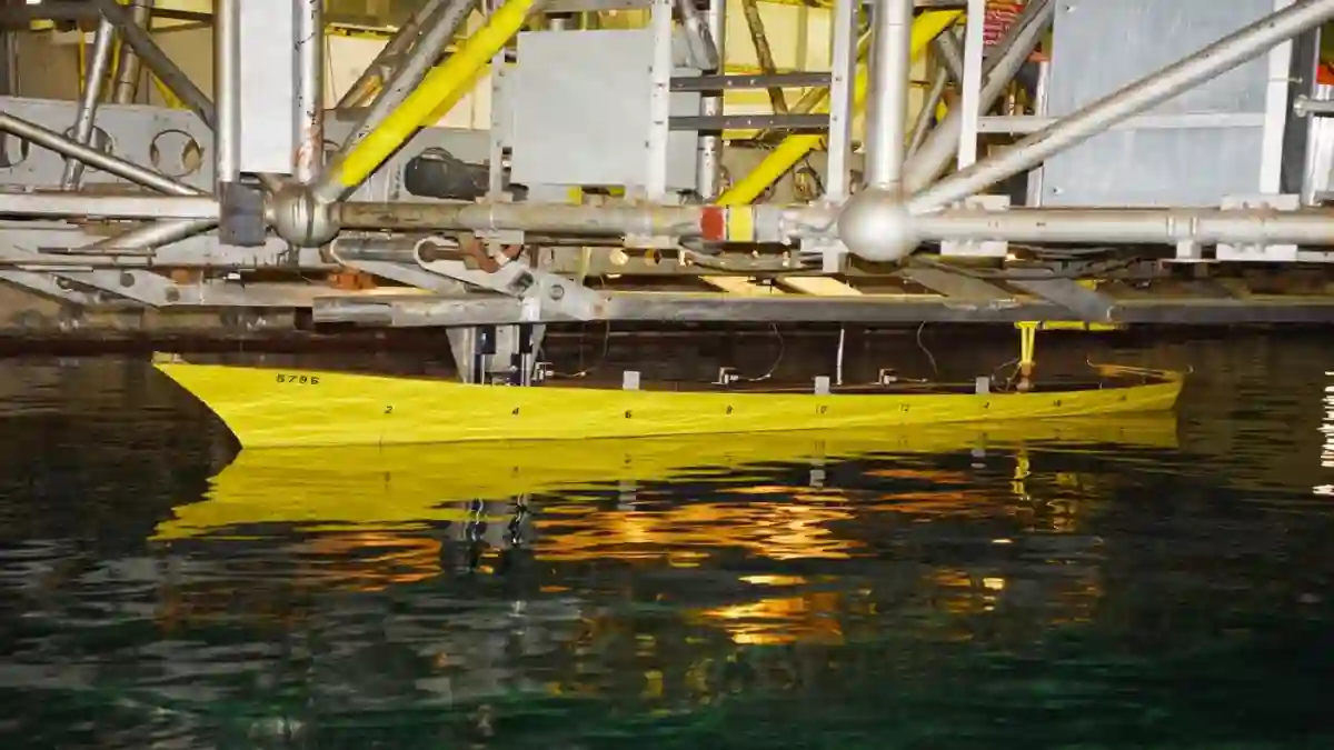Yellow scale ship model undergoing hydrodynamic testing in a towing tank